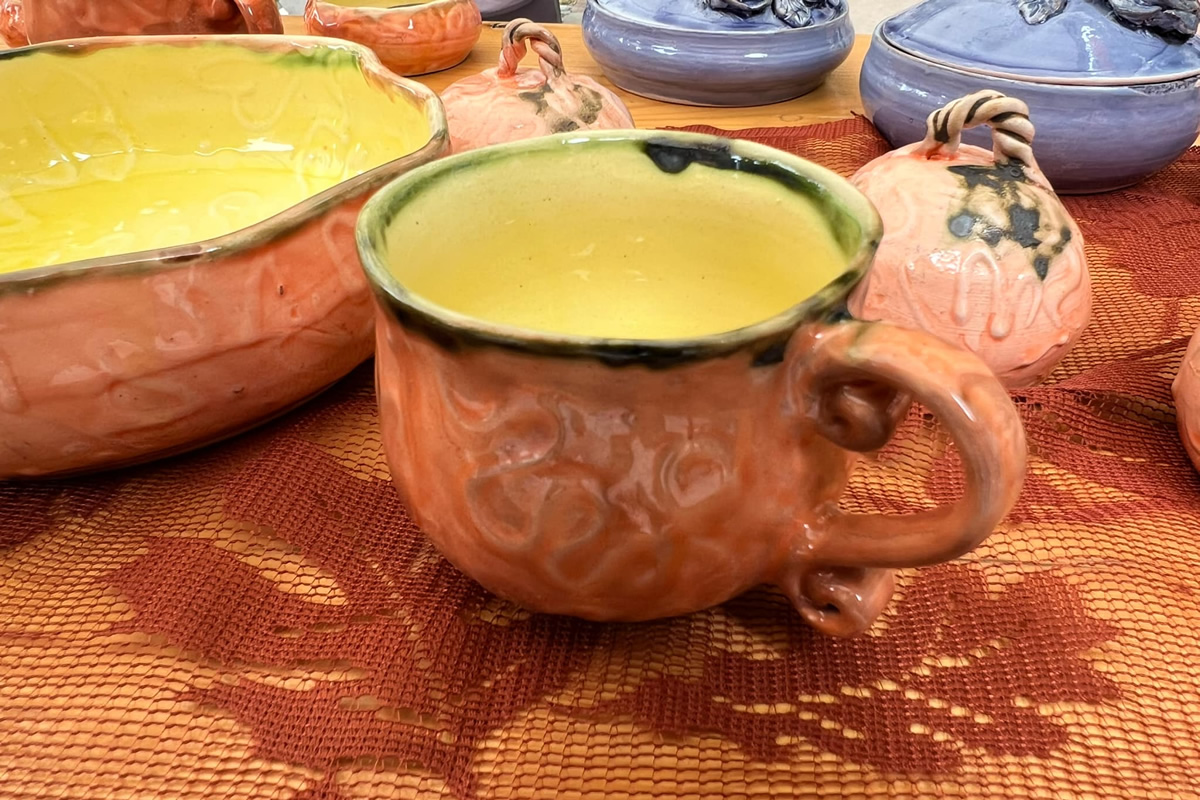 A beautiful handmade, vibrantly colored mug placed on a table with other ceramics.