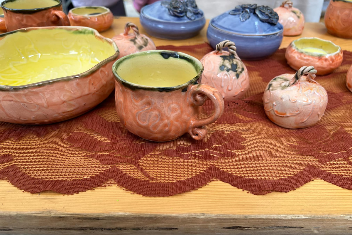A beautiful handmade, vibrantly colored mug placed on a table with other ceramics. That's an interesting merch mug idea.