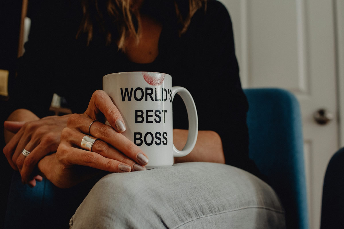 A woman sitting on a chair holding a mug saying - World's best boss.
